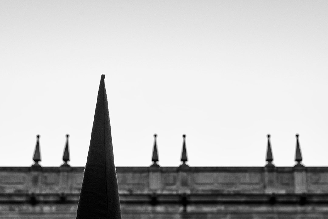 El pico de un capirote ante un edificio de piedra.
